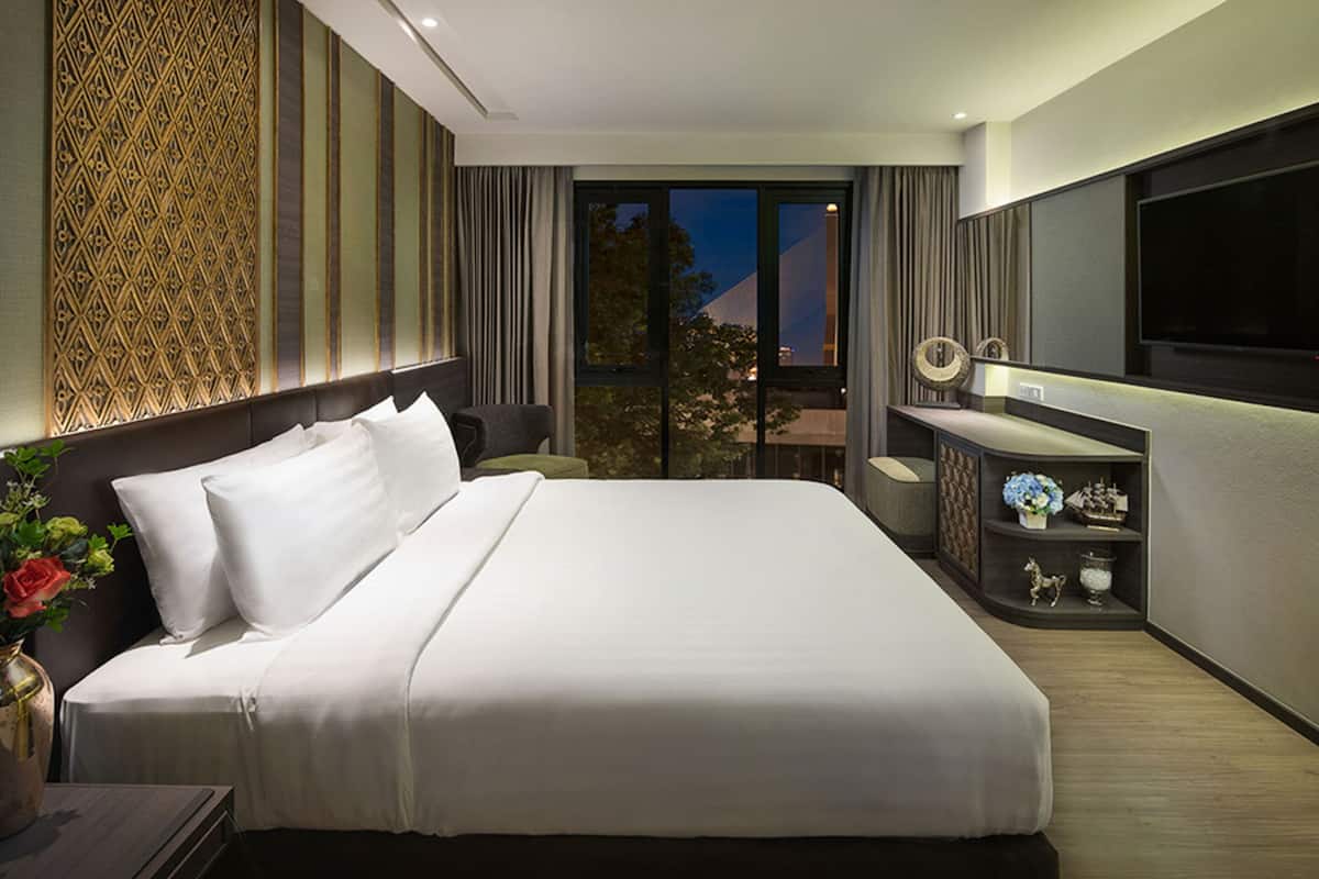 A modern hotel room with a large bed, a flat-screen TV, a small desk, and a view of the city at night.