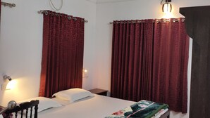 A room with a bed, a chair, a desk, a ceiling fan, and a wall-mounted air conditioner. - Kuttickattil Gardens Home Stay (Kottayam)