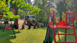 A playground with swings and a slide, surrounded by potted plants and a parked vehicle. - Kuttickattil Gardens Home Stay (Kottayam)