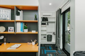 A modern room with a wooden desk, bookshelves, a small plant, a clock, and a bathroom with a shower curtain. - Redhill Cairns Shared Living – Pembroke St (Parramatta Park)