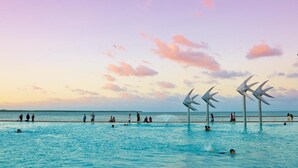 A swimming pool with people enjoying the water, surrounded by a pier with wind sculptures. - Redhill Cairns Shared Living – Pembroke St (Parramatta Park)