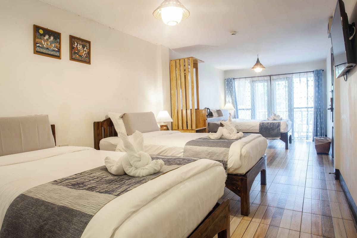 Ein Hotelzimmer mit drei Betten, jeweils mit Handtuch und Decke. Zwei an der Wand befestigte Fernseher und ein Holztrenner sind vorhanden.