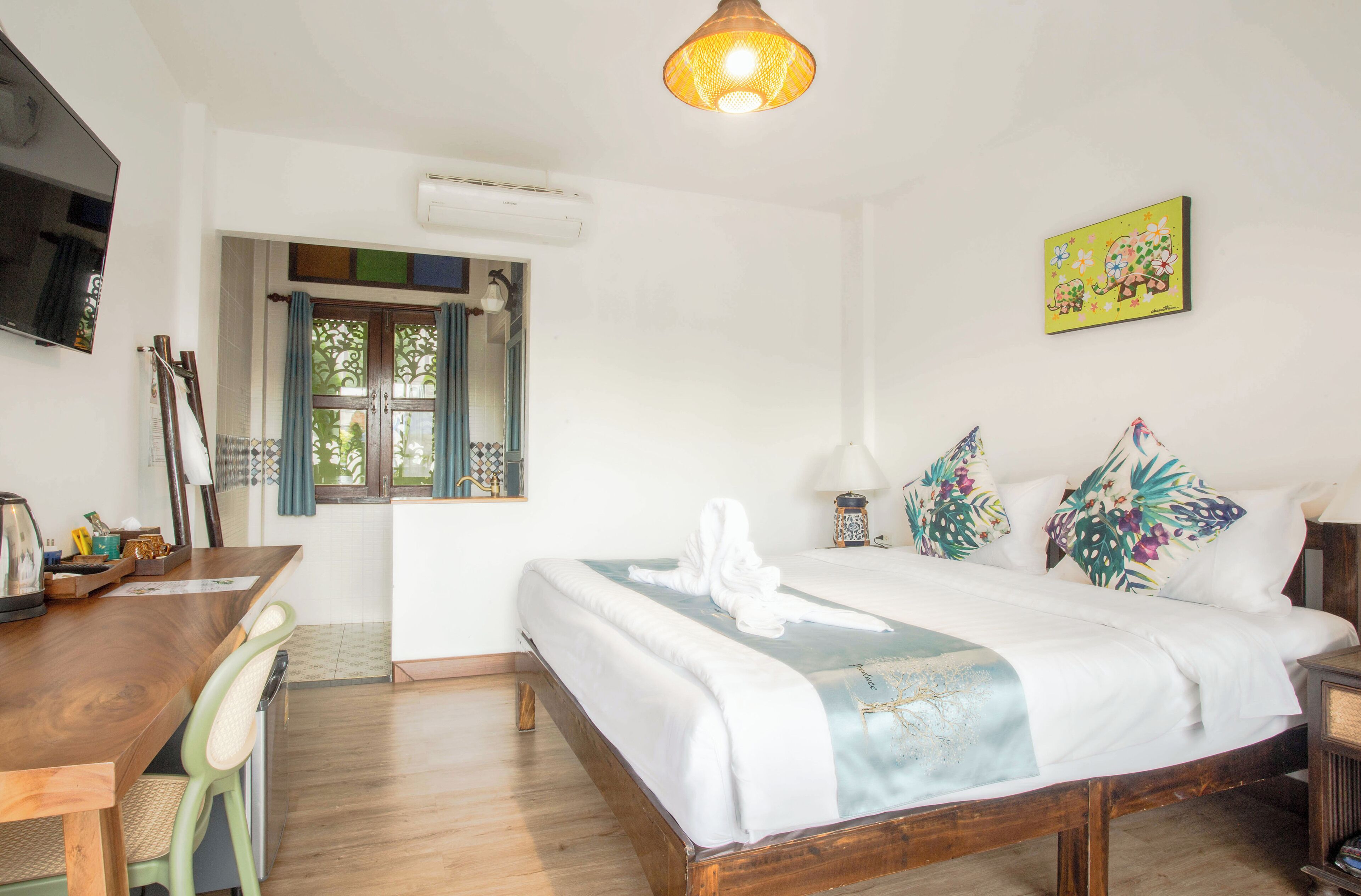 A bedroom with a wooden bed, a desk, a chair, a TV, and a window with curtains.