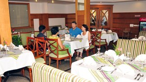 A restaurant with multiple tables and chairs, some with green cushions. - V K G Group Holiday Hotel (Kochi)