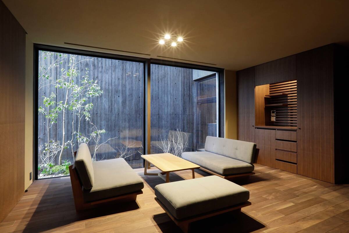 Een moderne woonkamer met een bank, twee fauteuils, een salontafel en een houten kast. Grote ramen bieden uitzicht op een tuin.