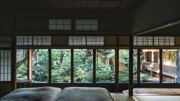 Ein traditioneller japanischer Raum mit Tatami-Boden, Futon-Bett und großen Fenstern mit Blick auf einen üppigen Garten.