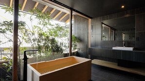 Un baño moderno con una bañera grande, baldosas oscuras y un ventanal con plantas.
