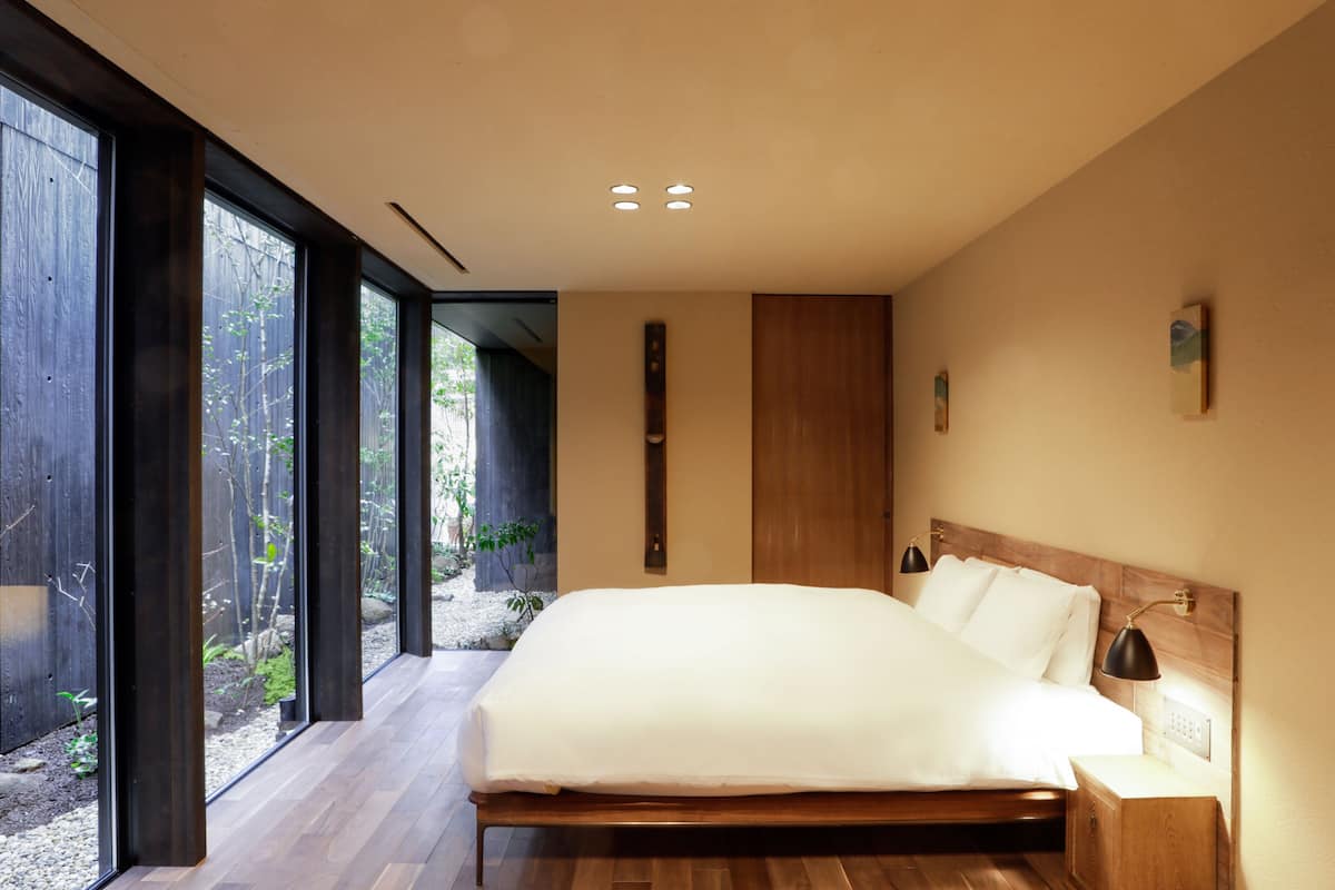 Een moderne slaapkamer met een groot bed, houten hoofdeinde en uitzicht op een tuin door middel van raamwanden.