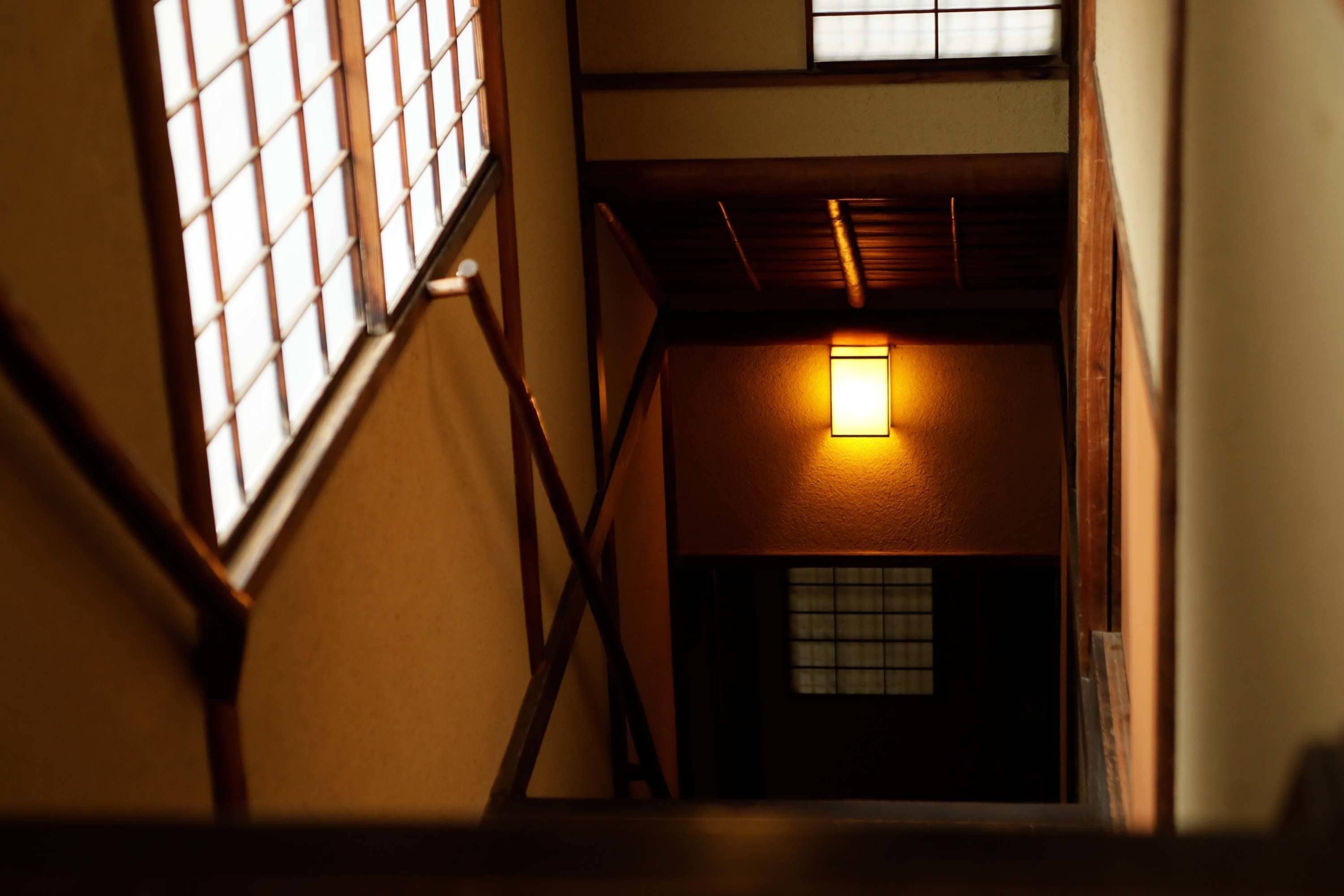 A staircase with wooden railings and a lit wall lamp.