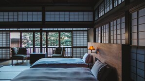 Una habitación tradicional japonesa con suelo de tatami, una cama baja de madera, una mesita y una silla.