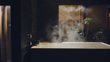A steam room with a large bathtub, a wooden door, and a plant in the background.