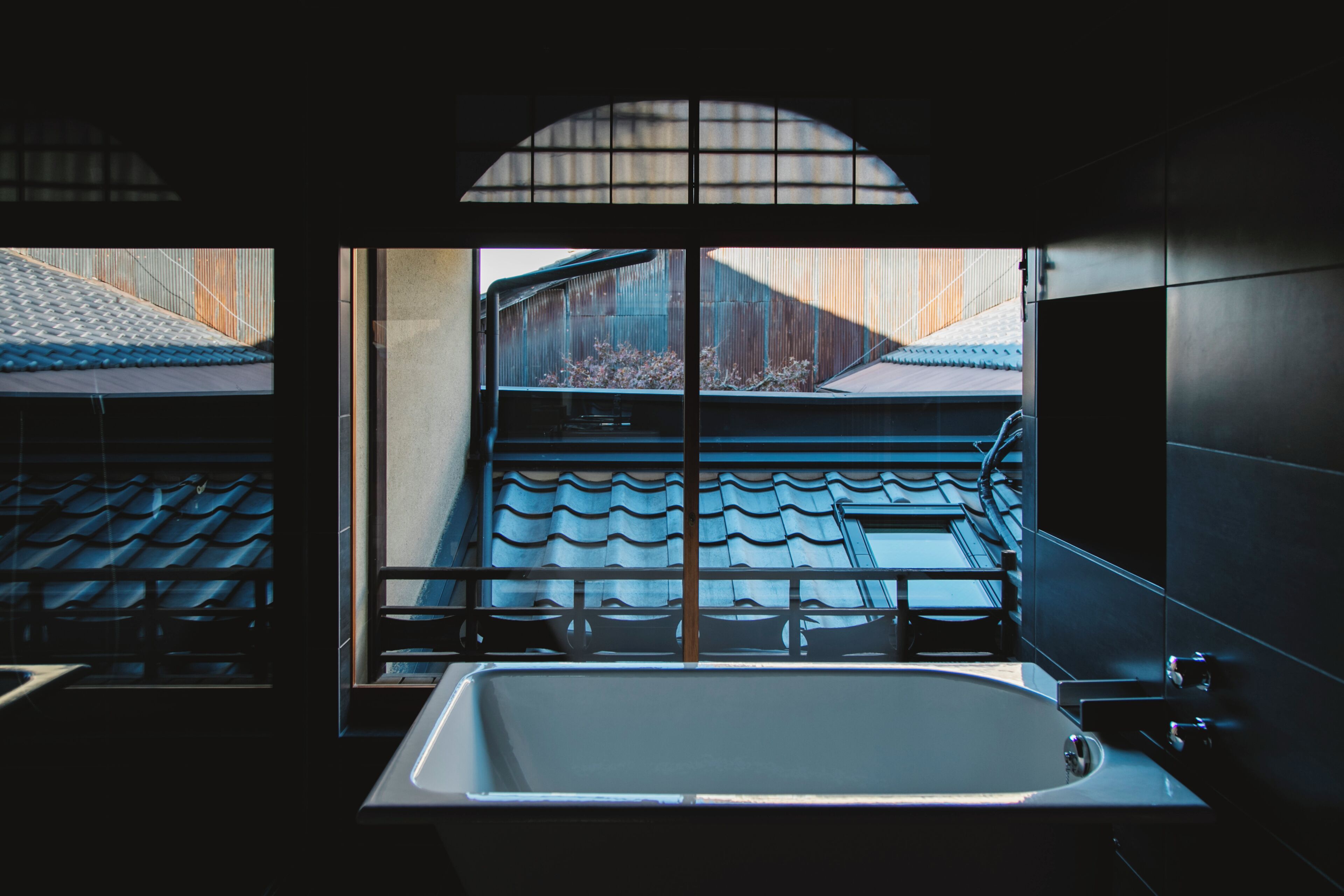 A modern bathroom with a large bathtub, a window with a view of a traditional building, and a tiled floor.
