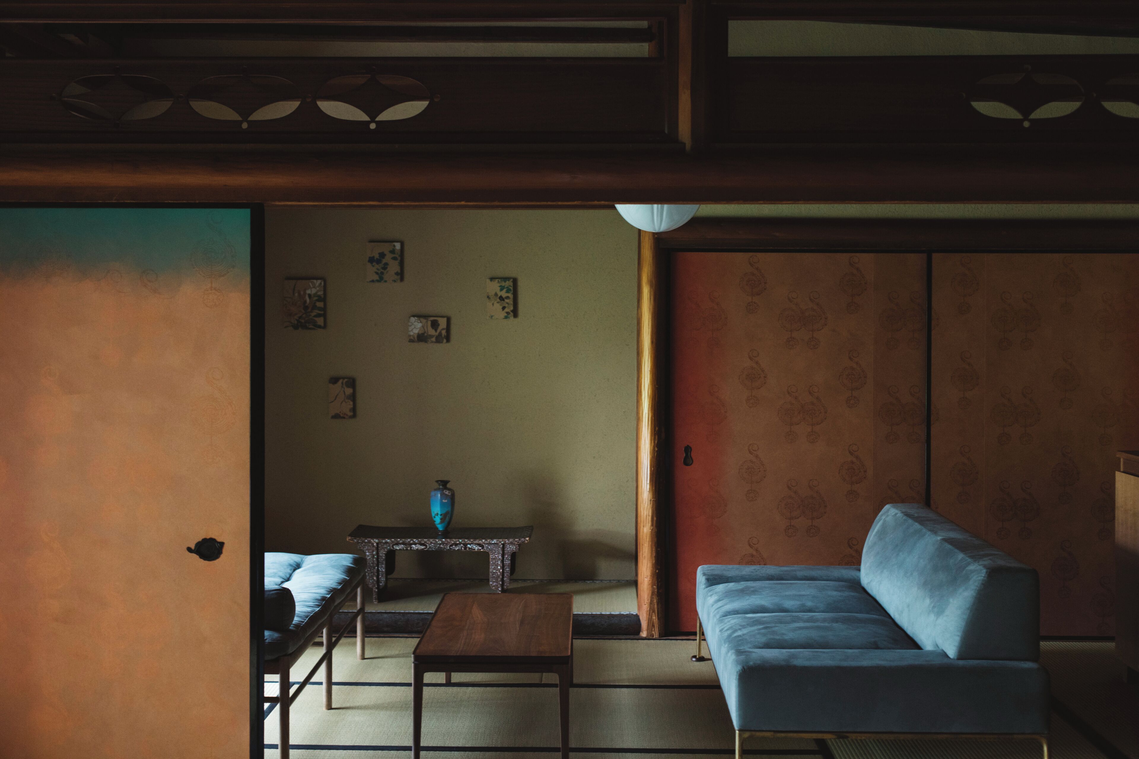 Een traditionele Japanse kamer met tatami vloerbedekking, een lage houten tafel, een blauwe bank en een schuifdeur.