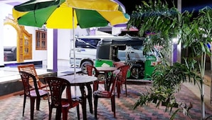 An outdoor seating area with tables and chairs, a green and yellow umbrella, and a tuk-tuk parked nearby. - SNP Star Guesthouse (Trincomalee)