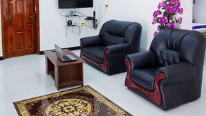 A living room with two black leather sofas, a wooden coffee table, a flat-screen TV mounted on the wall, a wooden door, and a decorative rug. - SNP Star Guesthouse (Trincomalee)