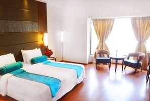 Habitación de hotel con una cama grande, dos sillas, una mesita, una mesita de noche y una ventana con cortinas.