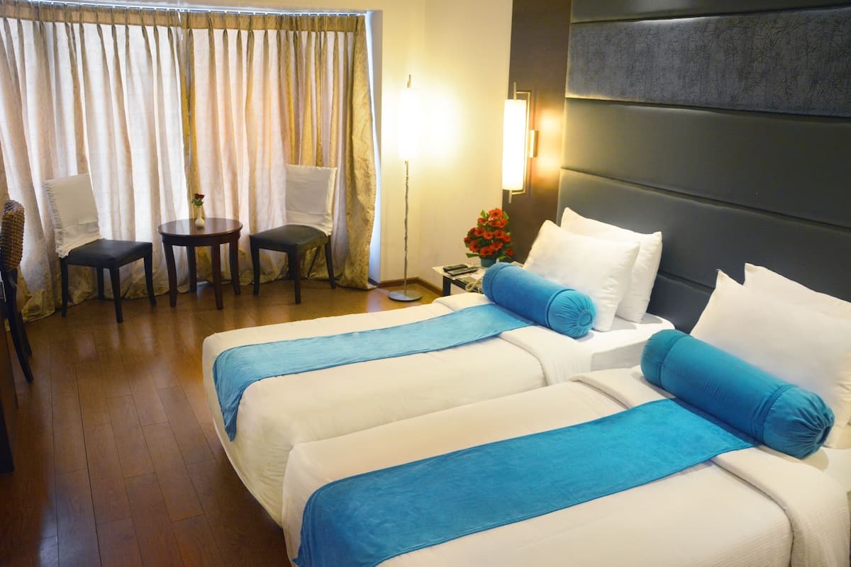 A hotel room with two beds, a desk, a chair, a lamp, and a window with curtains.