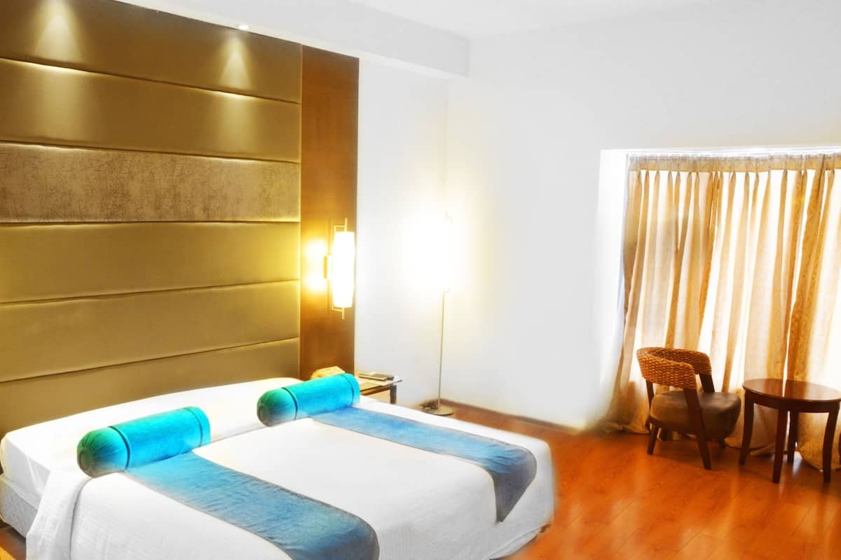 A hotel room with a large bed, a bedside table, a lamp, a chair, and a small table.