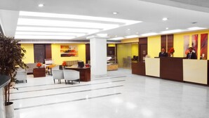 A modern hotel lobby with a reception desk, seating area, and a large plant. - Ashraya International Hotel (Bengaluru)