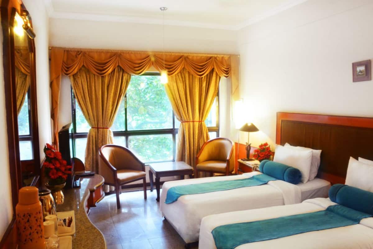 A hotel room with two beds, a sitting area with chairs, a small table, and a window with curtains.