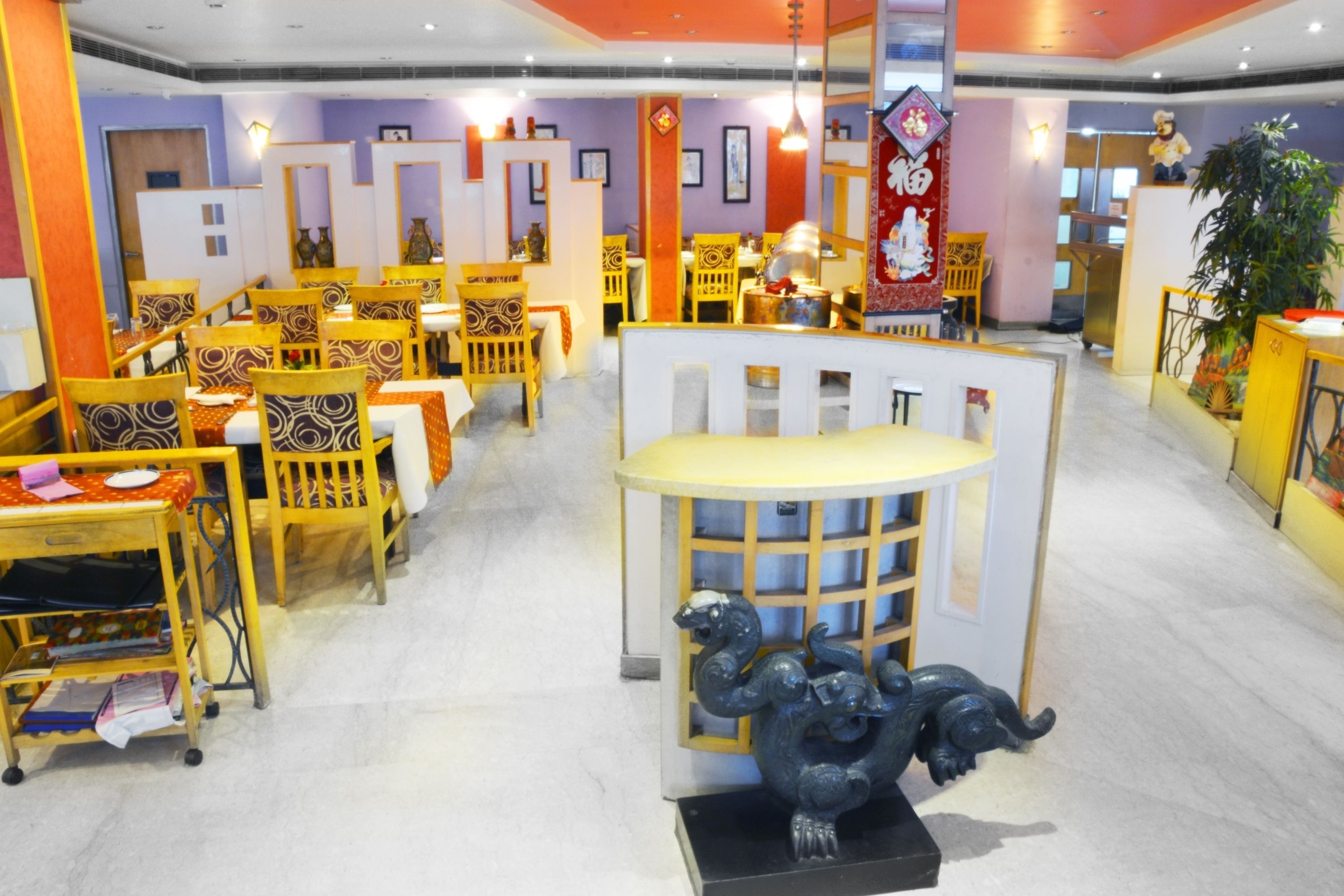 A restaurant with multiple dining areas, each with wooden chairs and tables. There are decorative elements like a blue elephant statue and a red hanging ornament.