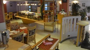 A restaurant with multiple tables, chairs, and a central buffet area. - Ashraya International Hotel (Bengaluru)