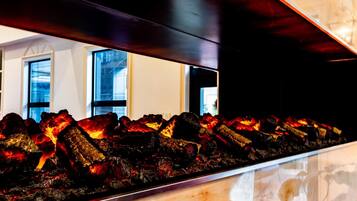 A charcoal grill with visible flames, set against a modern interior with large windows and a wooden ceiling.