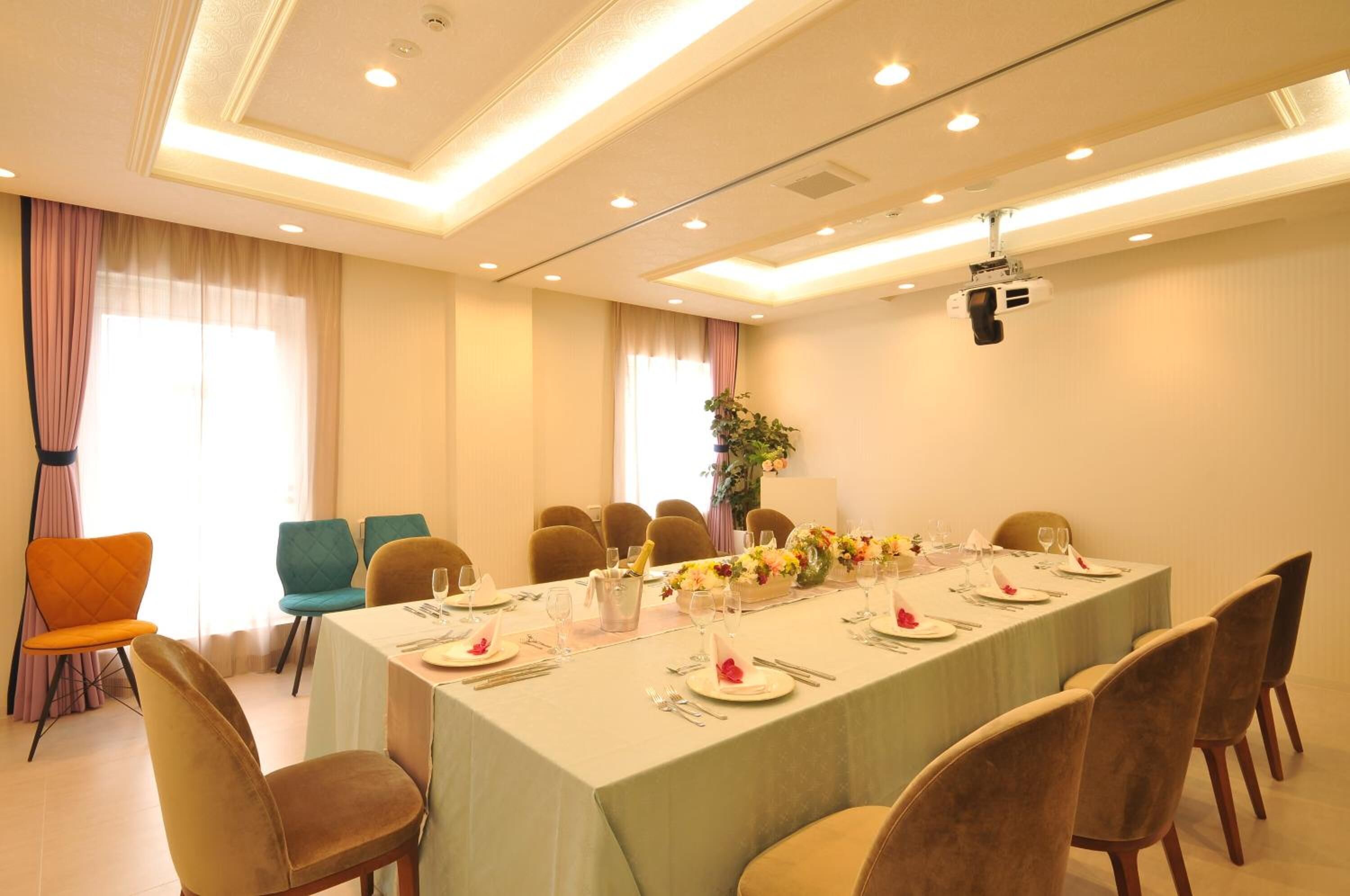 A conference room with a long table set for a meeting, surrounded by chairs, and a projector mounted on the ceiling.