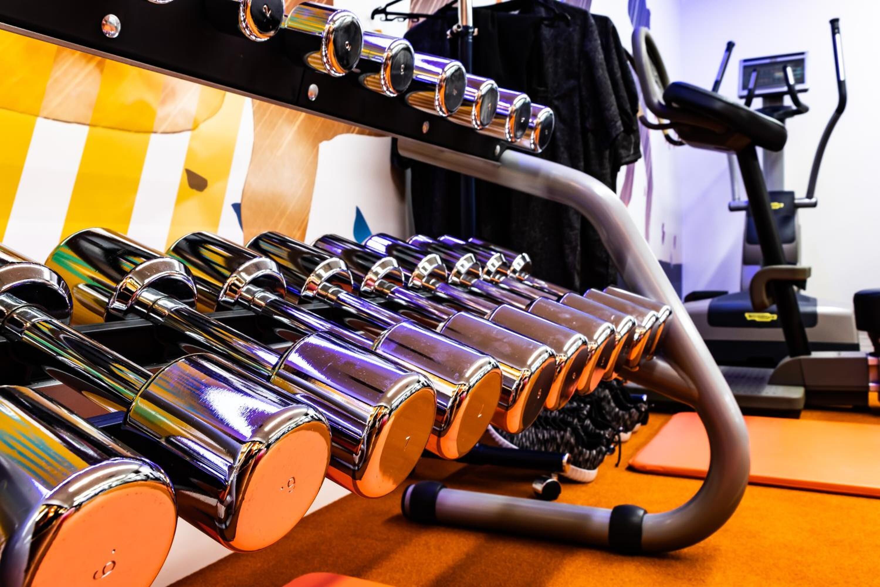 A row of shiny, metallic dumbbells on a curved rack in a gym setting.