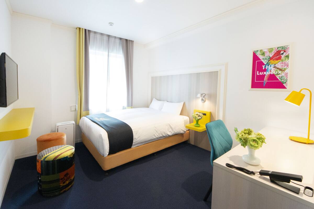Una habitación de hotel con cama, mesita de noche, silla, escritorio, lámpara y un adorno en la pared.
