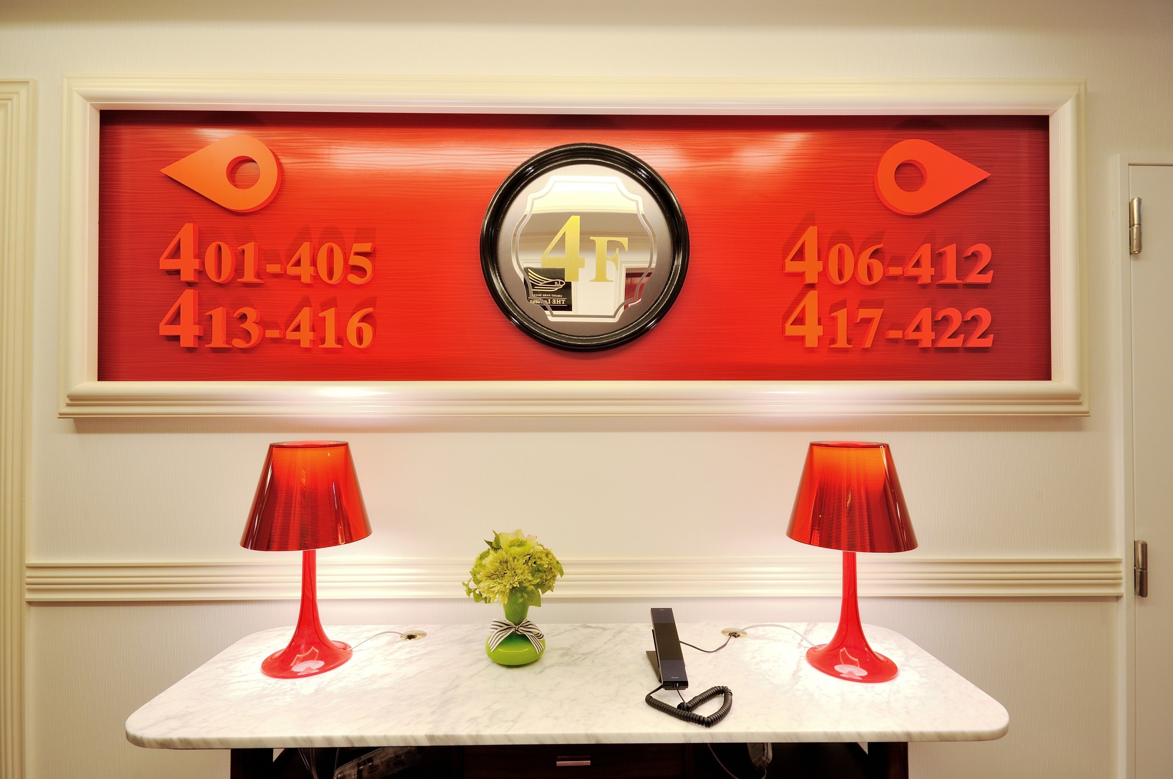 A reception desk with a red telephone, a vase with flowers, and a framed number display.