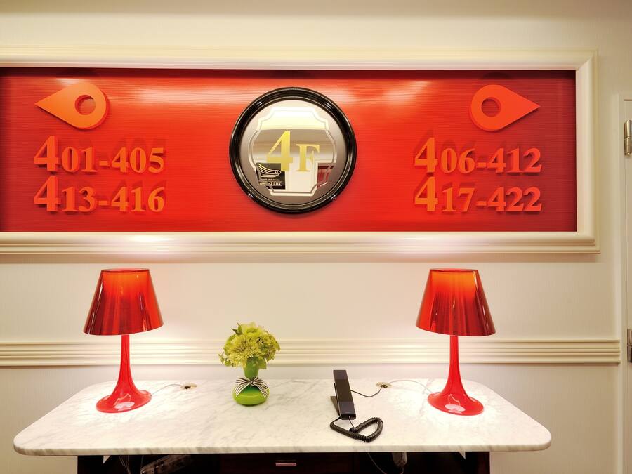 A reception desk with a red telephone, a vase with flowers, and a framed number display.