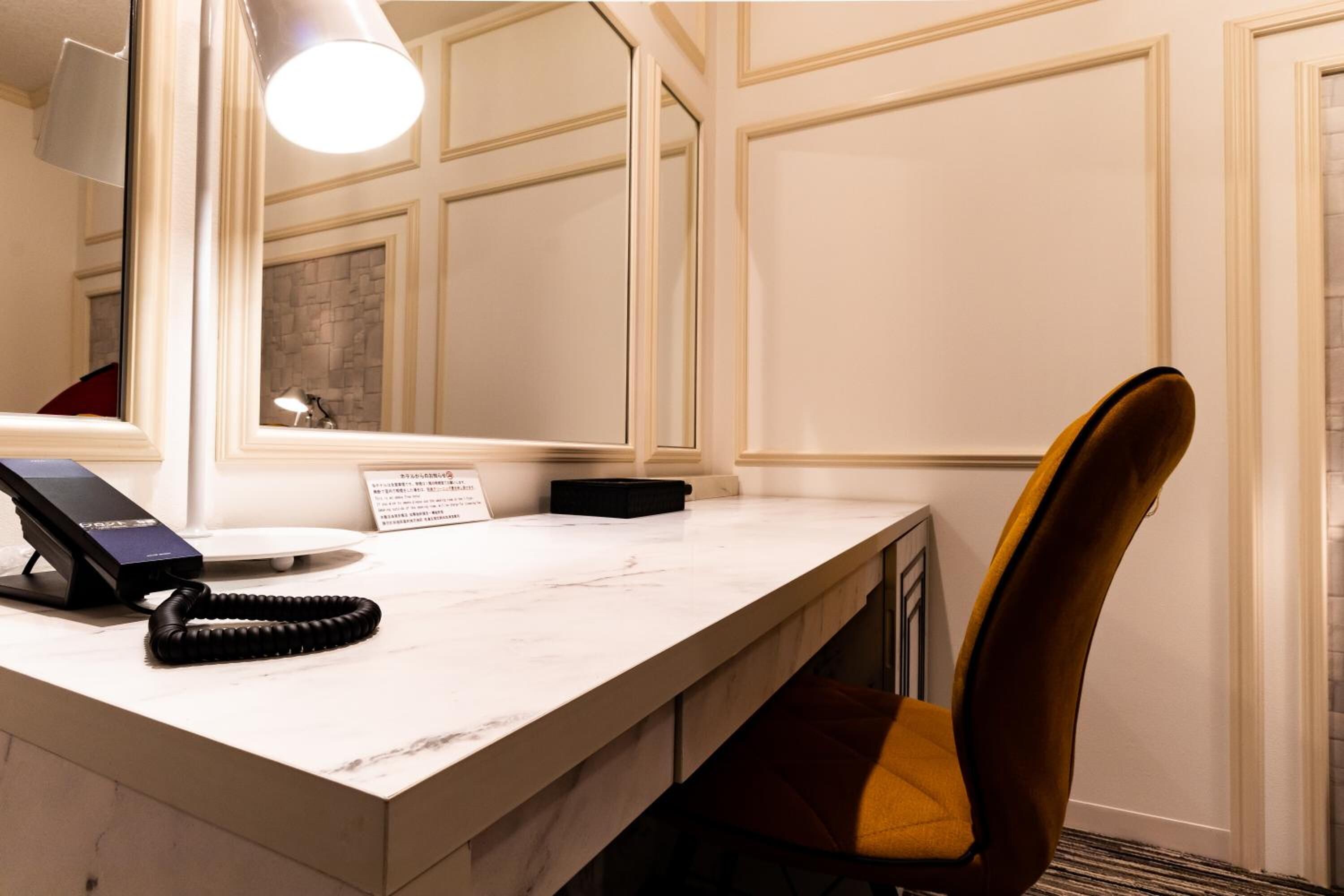 Habitación de hotel con escritorio de mármol, teléfono, silla y espejo.