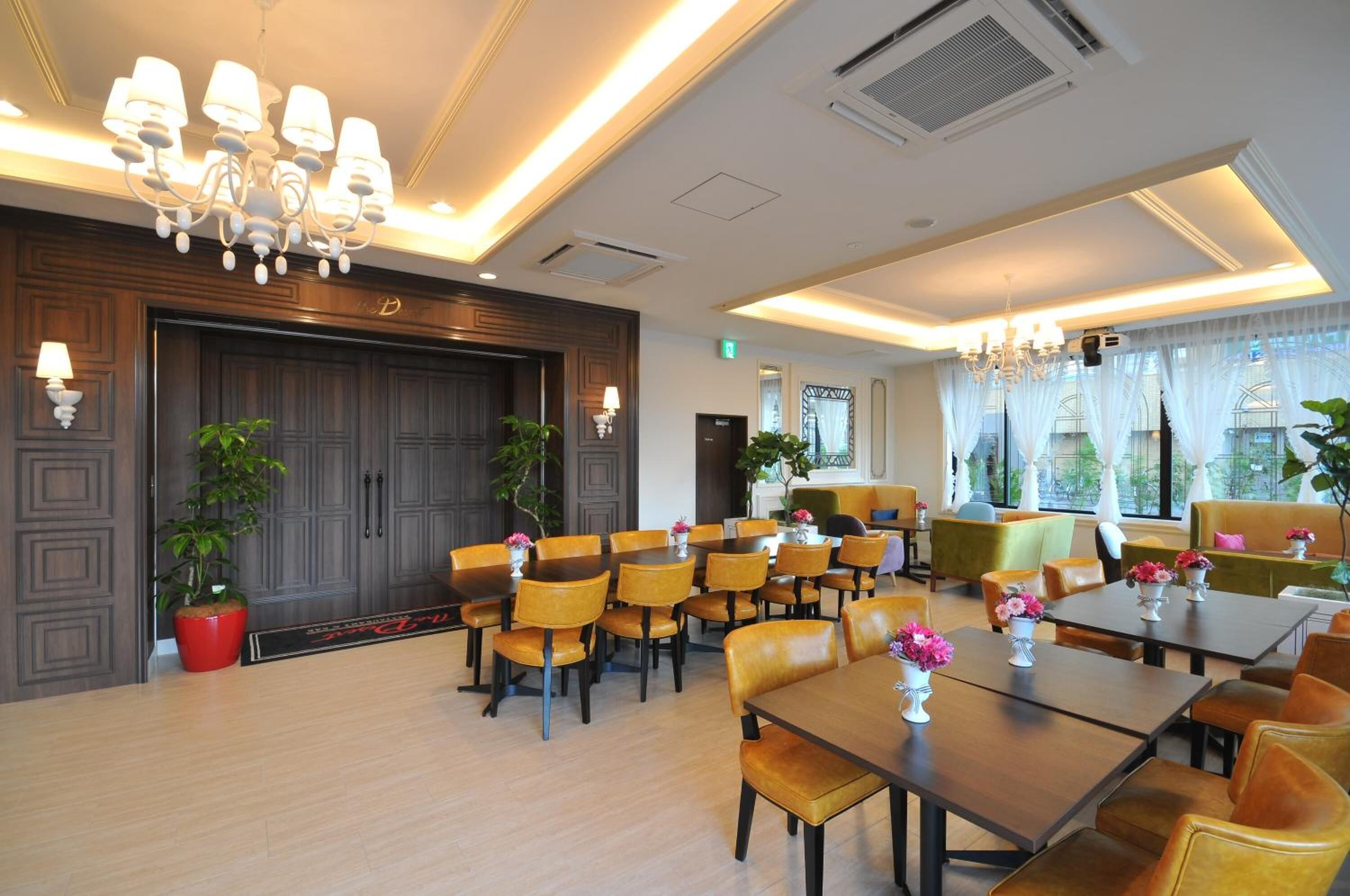 Ein Speisesaal eines Hotels mit Holztischen und -stühlen, einem Kronleuchter und Topfpflanzen.
