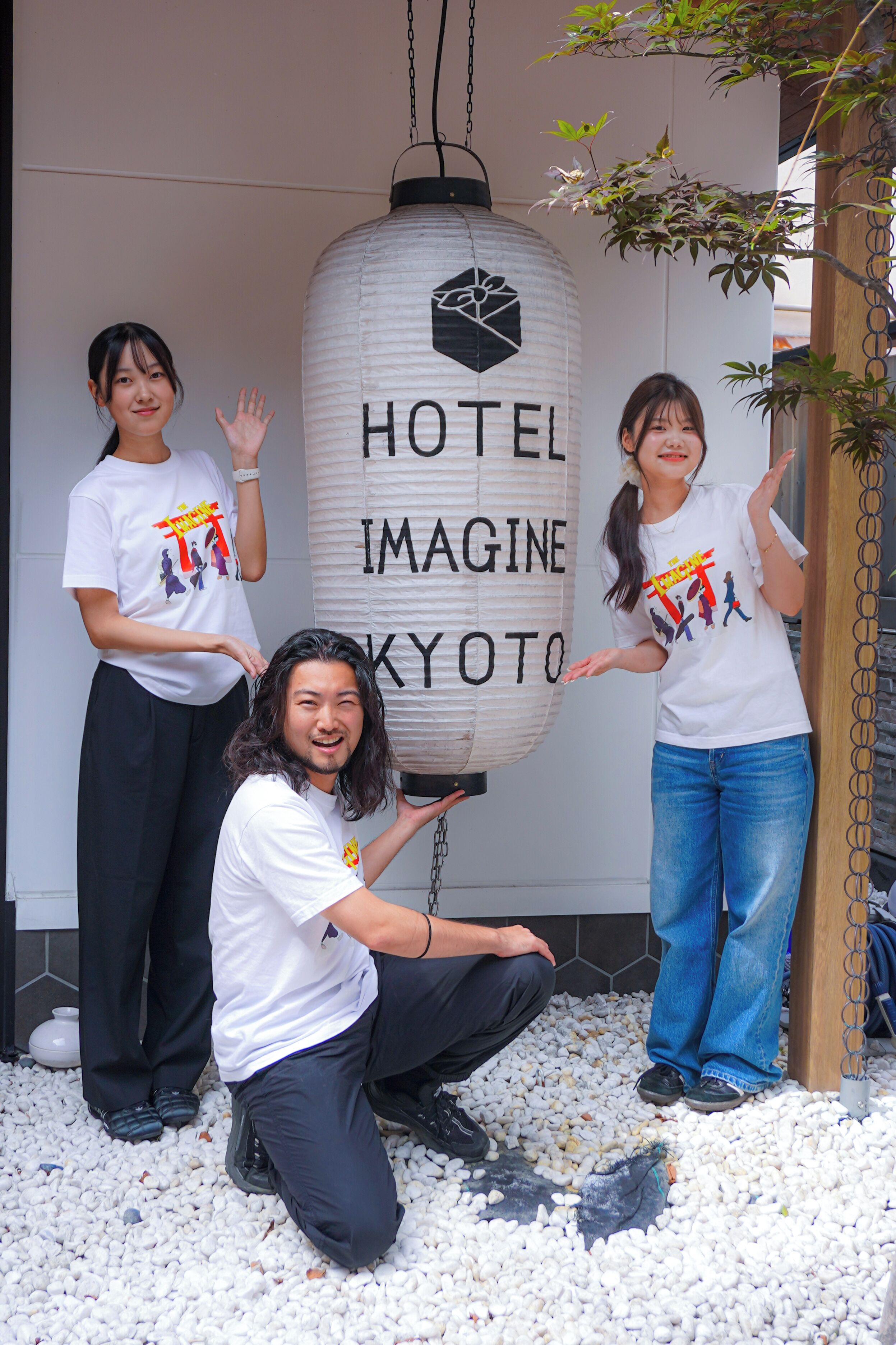 A group of people standing in front of a large white sign with 'HOTEL IMAGINE KYOTO' written on it.