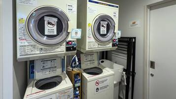 A laundry facility with two front-loading washing machines, a dryer, and a small ironing station.