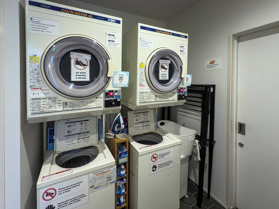 A laundry facility with two front-loading washing machines, a dryer, and a small ironing station.