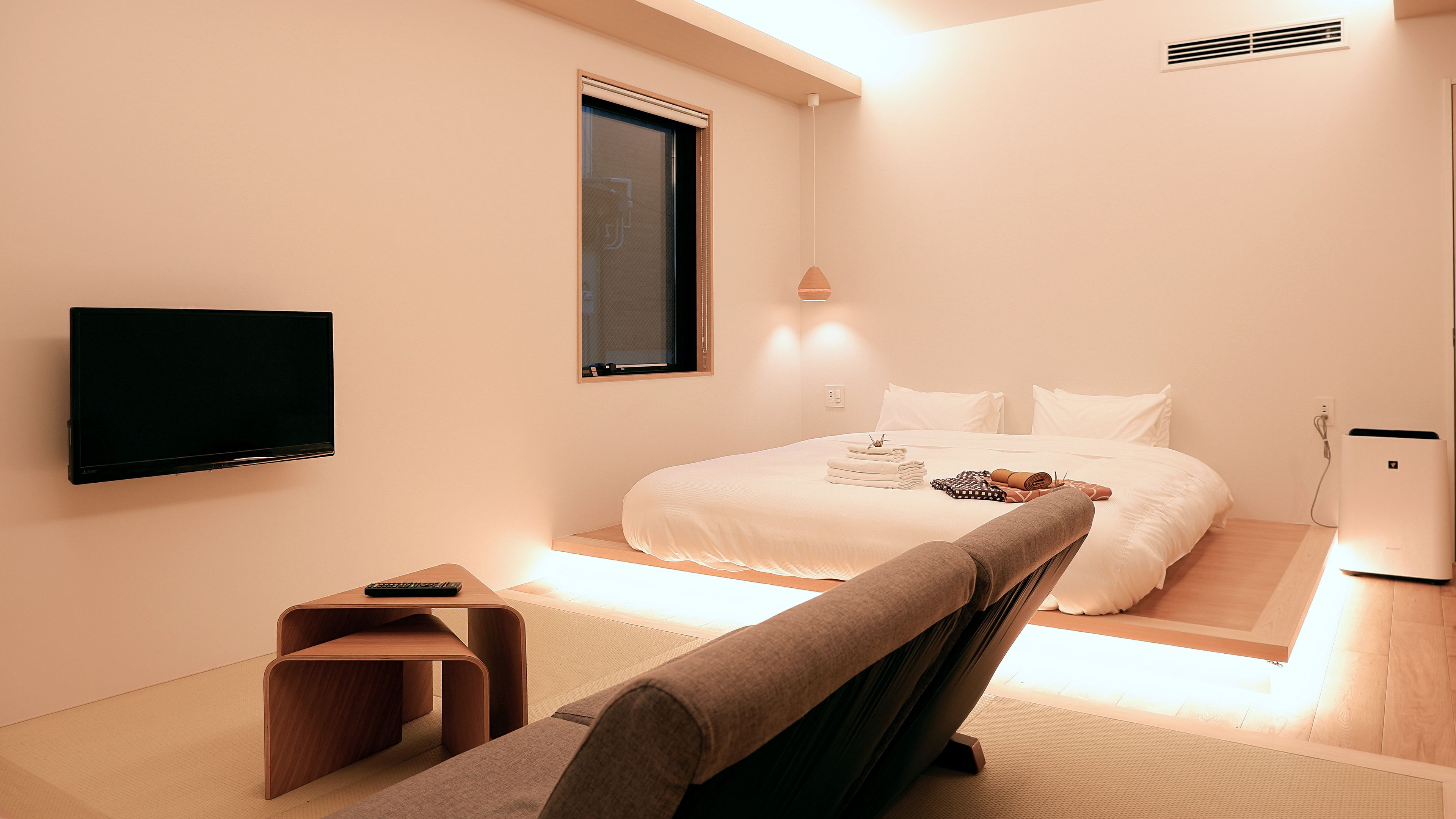 A modern hotel room with a bed, a TV, a desk, and a chair.