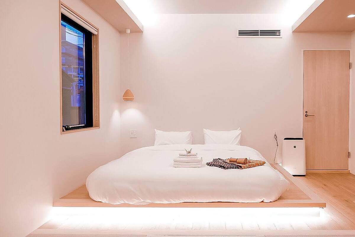 Une chambre à coucher au style minimaliste, avec un grand lit, une table de chevet, une armoire et une fenêtre équipée de stores.