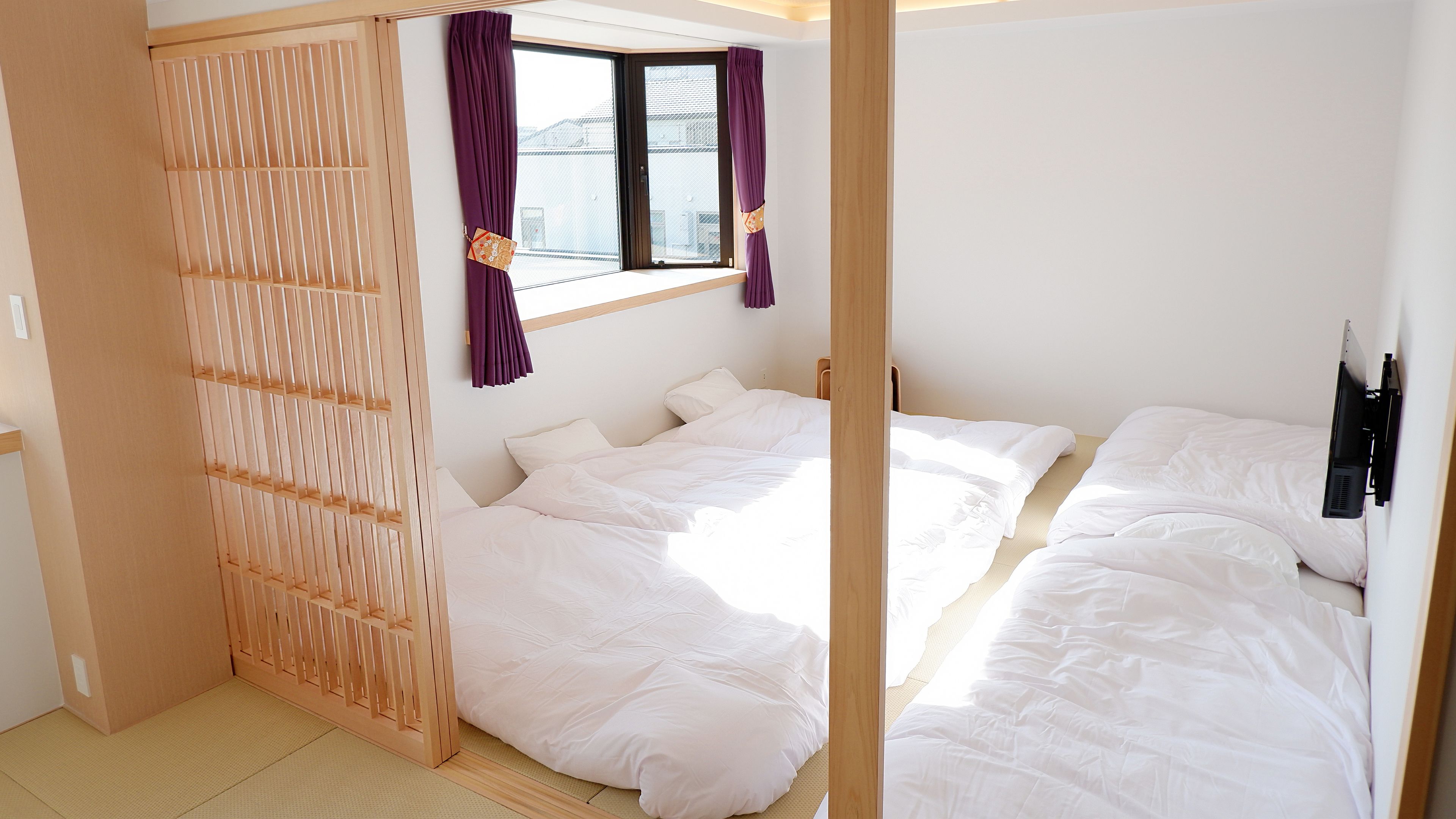 A room with two beds, a window with purple curtains, and a wooden partition.