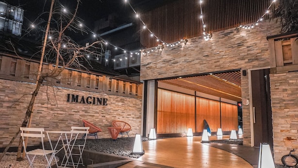 Un espacio al aire libre con un banco de madera, una mesa y sillas. Hay un letrero que dice