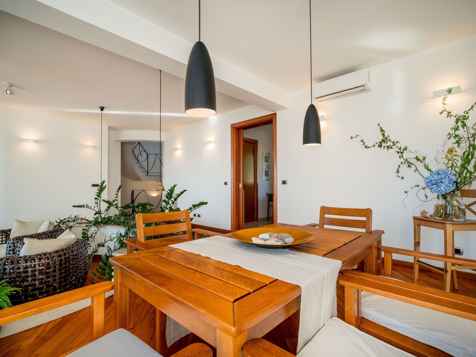 Un espace repas moderne avec une table et des chaises en bois, des luminaires suspendus et des plantes en pot.