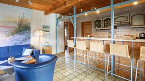 A cozy room with a blue sofa, a dining area with wicker chairs, and a kitchen with wooden cabinets and a tiled backsplash. - Stunning private villa for 5 guests with TV, patio and pets allowed (Otterndorf)