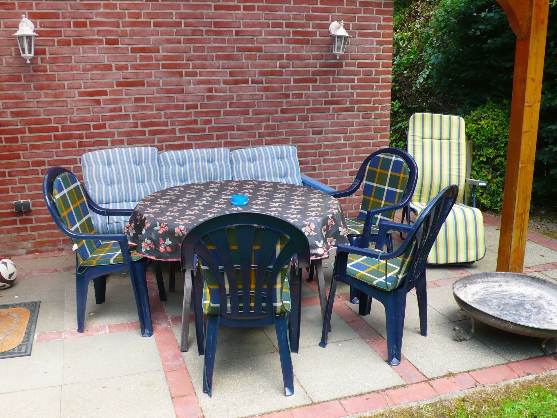 A patio with a round table and chairs, a brick wall, and a wooden pergola.