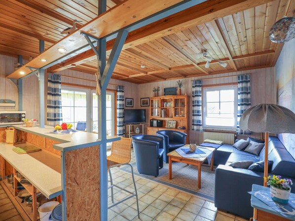 A cozy cabin interior with a dining area, seating, a television, and a bookshelf.