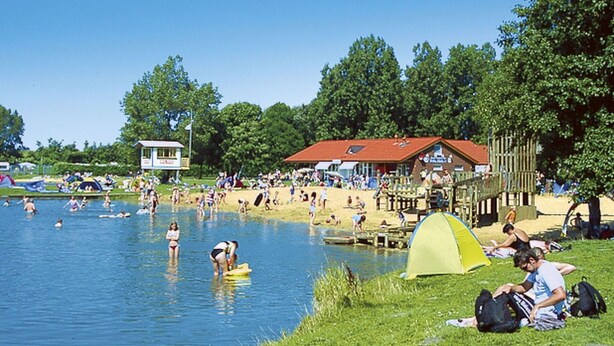 A lakeside scene with a grassy area, a yellow tent, and a building with a red roof. - Stunning private villa for 5 guests with TV, patio and pets allowed (Otterndorf)