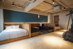 A modern hotel room with a large bed, a sofa, and a small seating area. There is a wooden headboard, a patterned wall, and a hanging light fixture. - SAUNALAND ASAKUSA - Hostel (Tokyo)