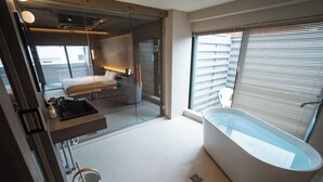 Un baño moderno con una bañera independiente, una cabina de ducha de vidrio y un amplio ventanal con persianas.