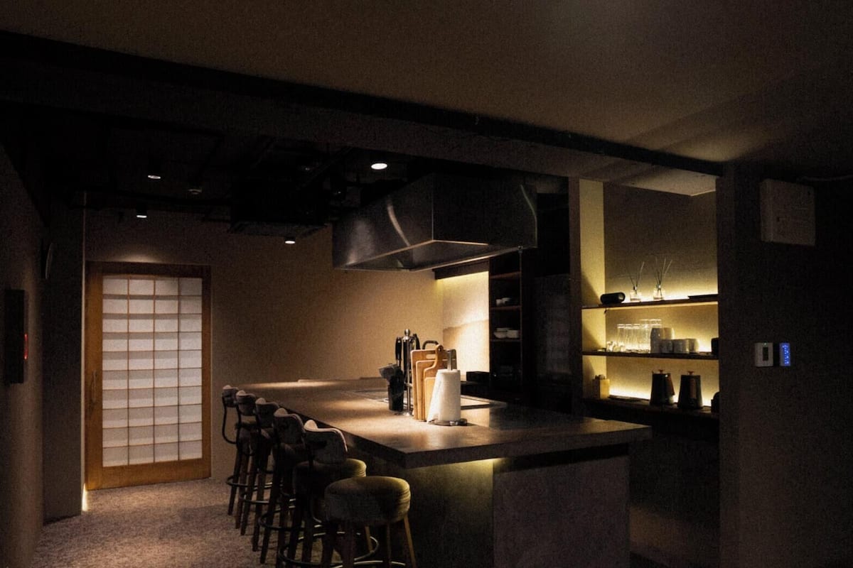 A dimly lit bar area with stools, a counter, and a large window with a grid pattern.