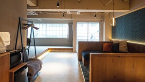 Una habitación de hotel moderna con un banco de madera, una pequeña kitchenette y un amplio ventanal que proporciona luz natural.